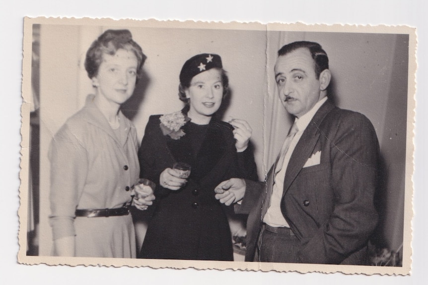 Two women and a man stand holding drinks and looking at the camera