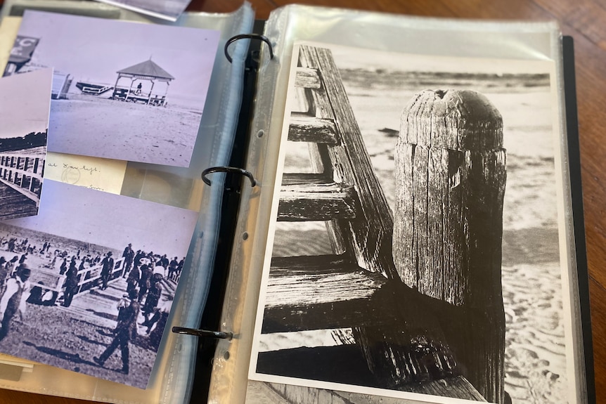 A page of a history book on a wooden table is seen with old black and white pictures of Altona Pier.