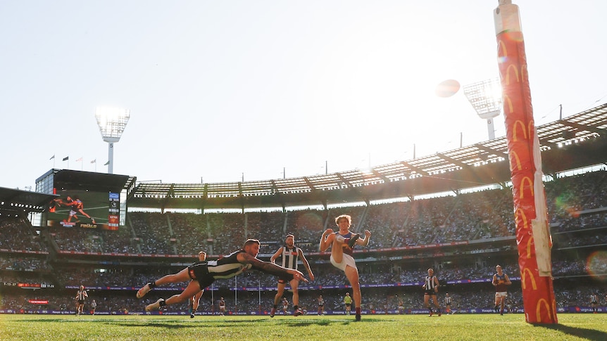 A view from behind the goal in the 2023 AFL grand final as Deven Robertson kicks a goal with the sun behind him.