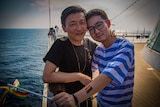 Two men stand smiling with their arms around each other on the deck of a cruise ship.