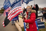 A woman in Trump glasses and a red coat, waving an American flag