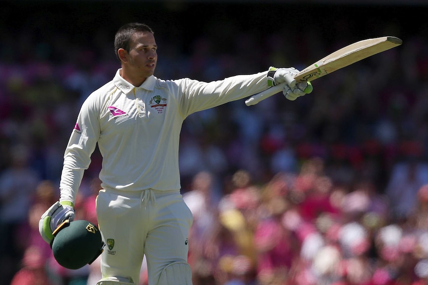 Usman Khawaja points his bat while holding his helmet in his other hand.