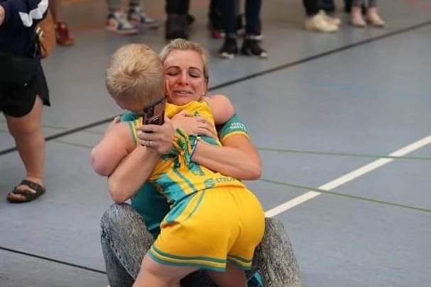 A young boy in an Australian sports uniform hugging his proud mum.