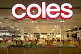 The front of a Coles supermarket. Underneath a large sign are displays of fruit and vegetables.