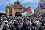 A large crowd of protestors outside Flinders Street Station. One student waves a Palestinian flag in the air.