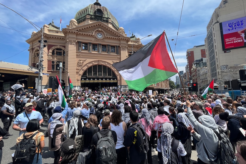 A large crowd of protestors outside Flinders Street Station. One student waves a Palestinian flag in the air.