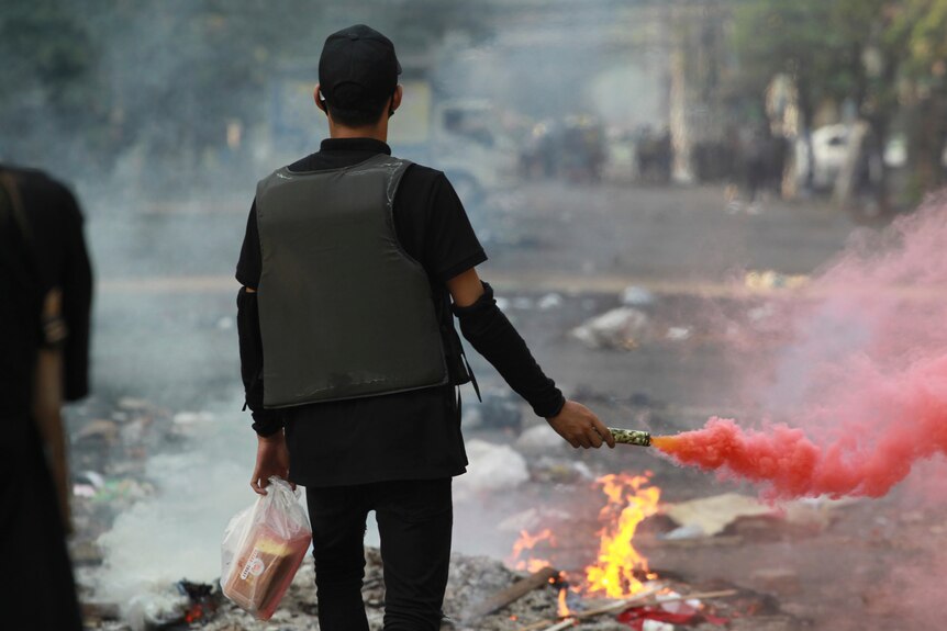 A protester holds a flare in his hand as he looks down the street towards a police line.