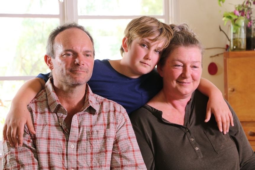 Woman and man are seated while boy stands behind them in the middle with arms around their shoulders.