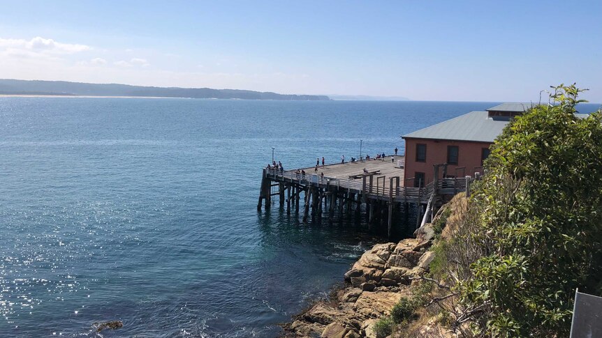 The ocean on the left and rocks, a building and a wharf on the right.
