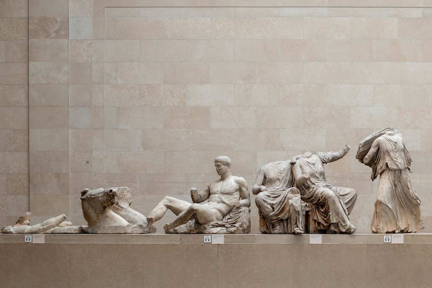 On a light tan plinth, you see a number of ancient Greek statues arranged in ascending height.