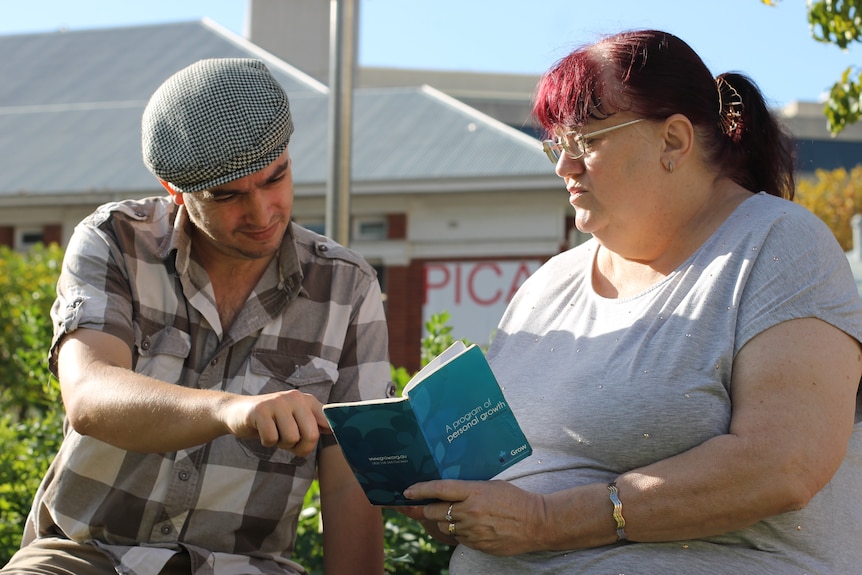 Man pointing to something in a small blue book being held by woman