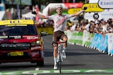 A cyclist wears a beaming smile as he spreads his arms wide in triumph crossing the finish line in a Tour de France stage. 