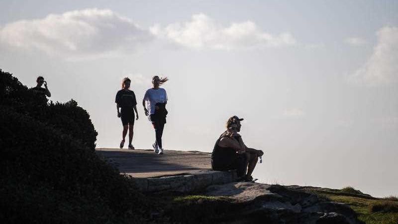 Two people walking next to a man sitting down on a cliff edge.