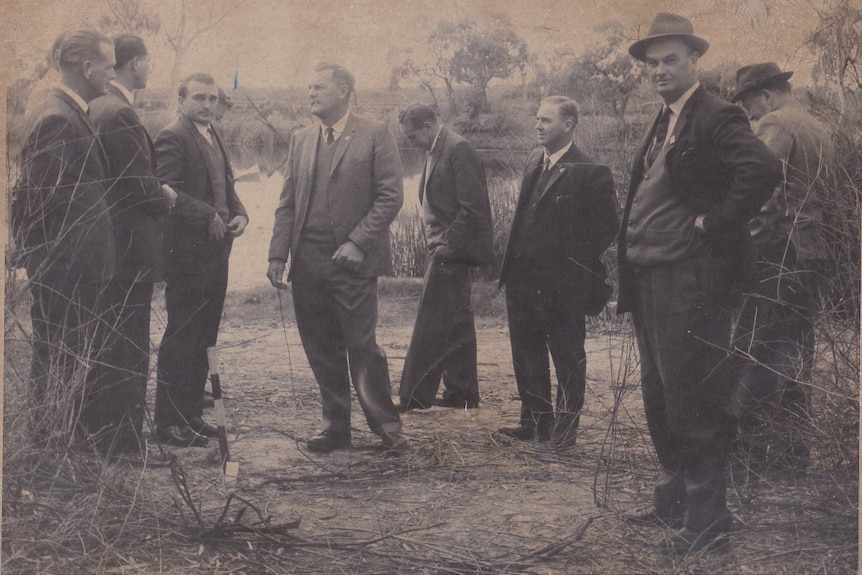 Men in suits standing in a paddock.