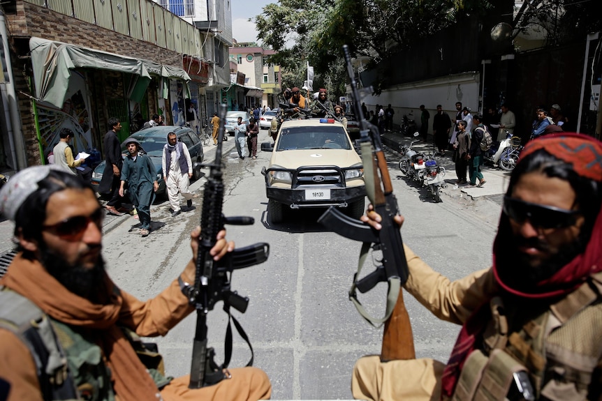 Two Taliban fighters sit holding their automatic rifles in the back of a truck patrolling Kabul