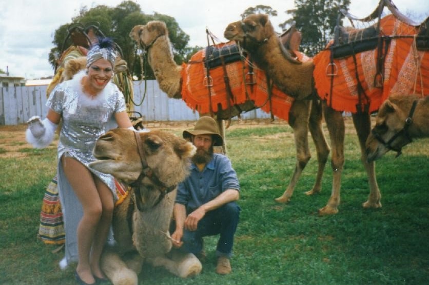 Fanny Cracker, dressed in a silver sequin gown sits on top of a camel.
