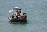 Four men in Australian military uniforms in a small rubber boat on the ocean.