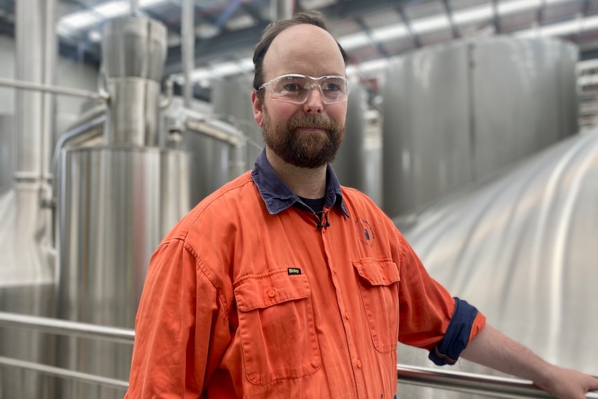 A man stands in a brewery surrounded by silver brewing machines