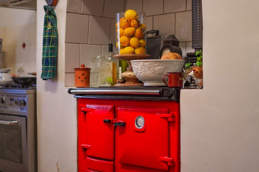 A bright red oven in a white kitchen with lemons and assorted jars and bowls above it.
