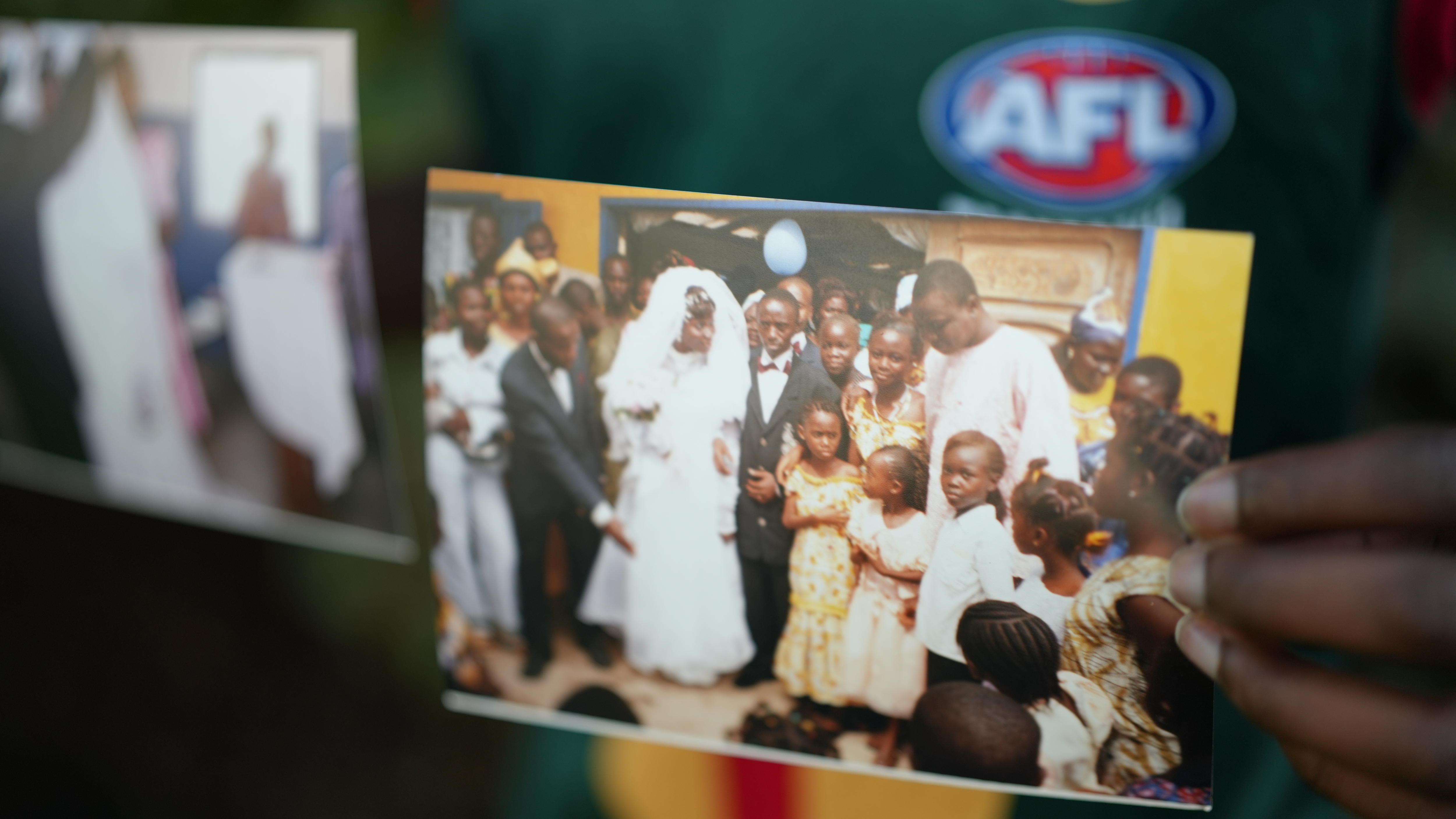 A photo of a hand holding two photos, one is blurry, one is of children crowding around a bride and groom.