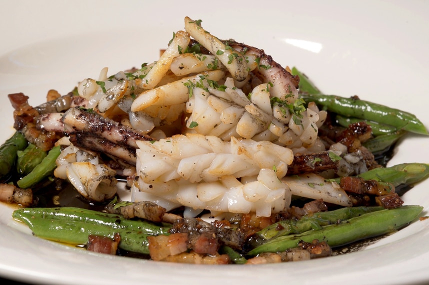 A plate displaying a finished recipe of squid with green beans and chilli pancetta to depict how to prepare and cook squid.
