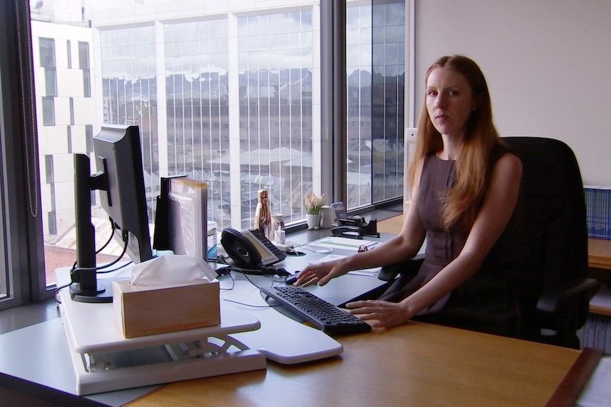 A woman with long brown hair sitting at a computer in an office