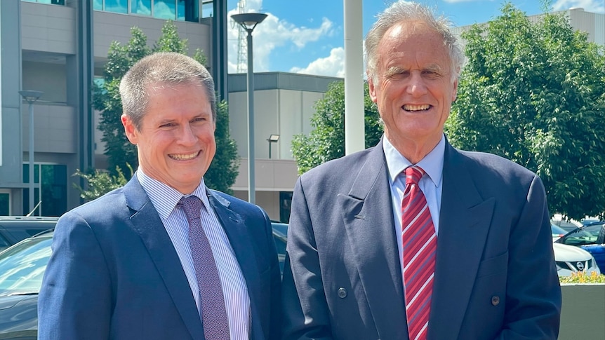 Two men standing side by side smiling.