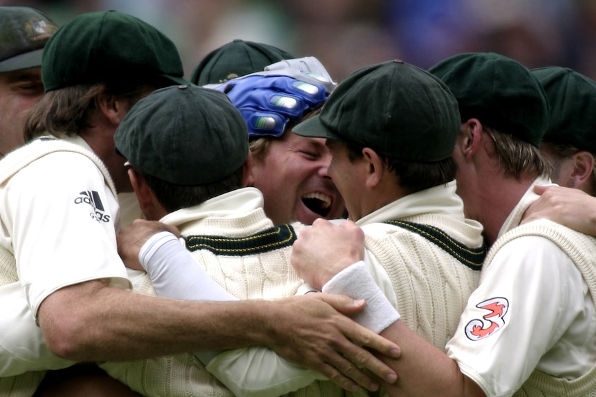 A beaming Shane Warne is surrounded by teammates in a congratulatory huddle