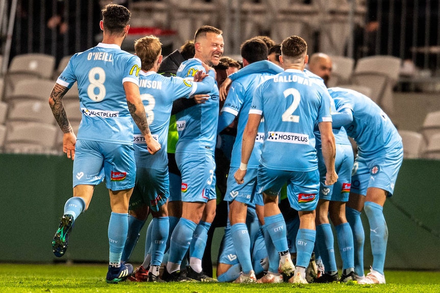 A group of Melbourne City A-League players embrace as they celebrate a goal.