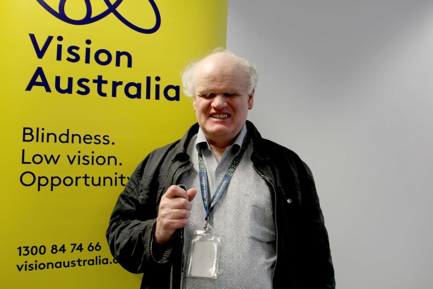 Bruce Maguire smiles in front of a Vision Australia banner.