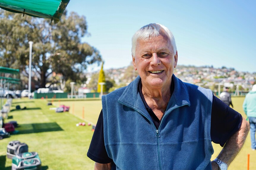 A man stands in front of a bowling green with one hand on his hip