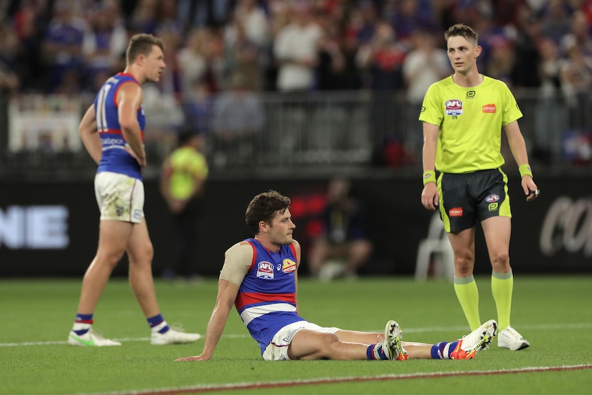 Western Bulldogs players look dejected as one sits on the turf after the siren in the AFL grand final.