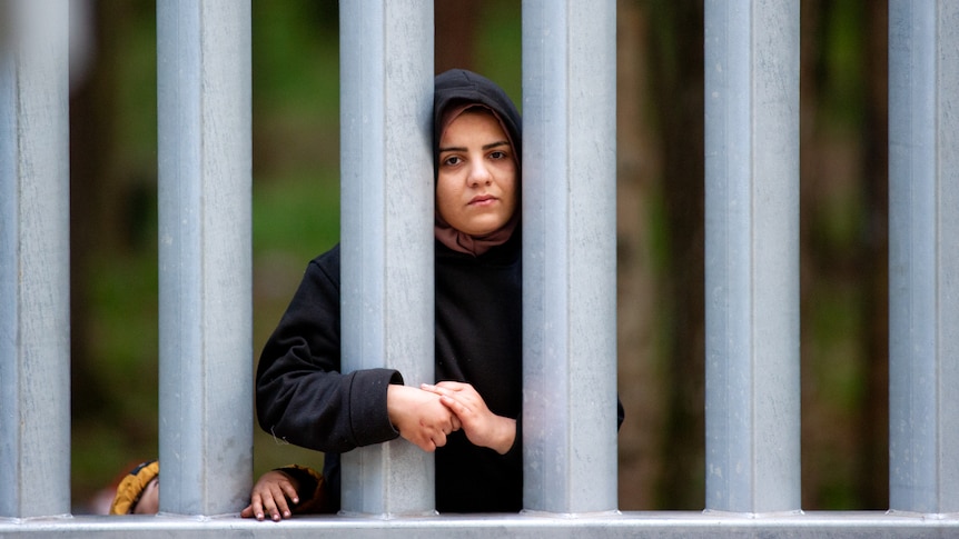 A young woman leans against the steel border force, looking into the camera. 