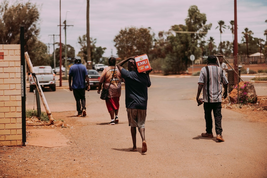 Four people walking away from a shop in an outback town, carrying alcohol.