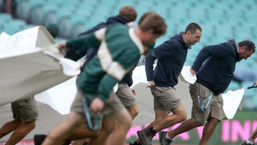 A shot from the side of a bunch of stewards dragging the covers on to the pitch.