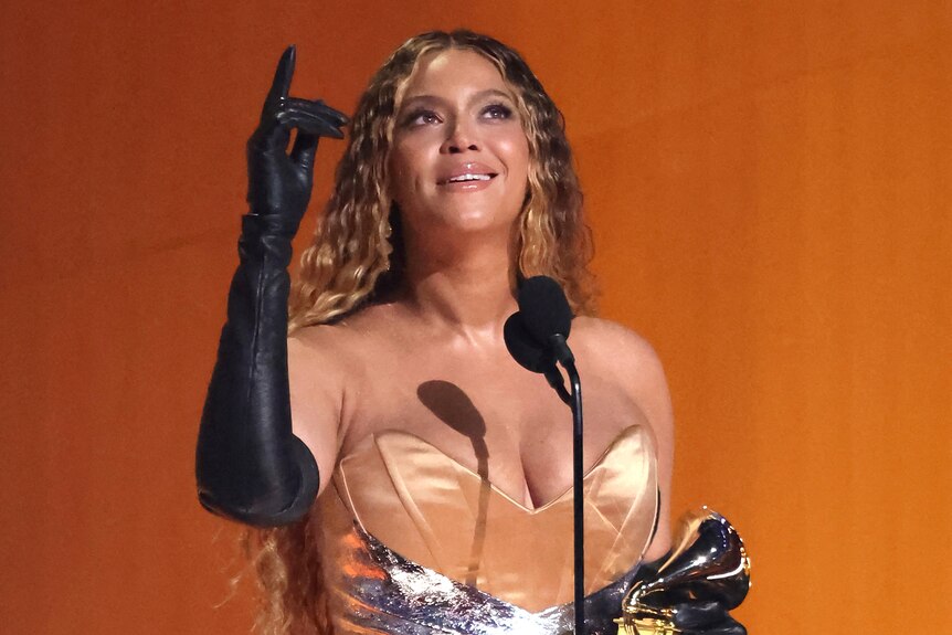 Beyonce on stage in front of microphone holding Grammy Award.
