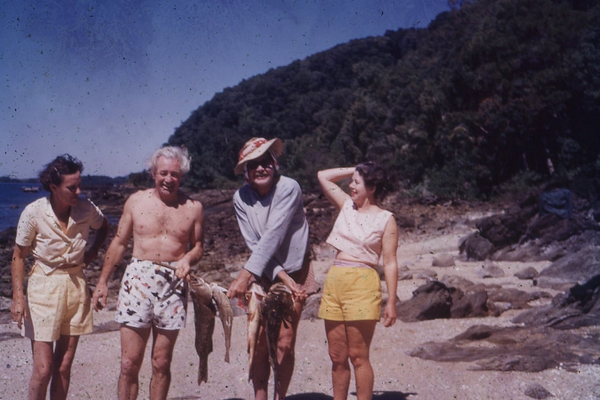 Allison Büsst (John's wife), Harold Holt, an unknown man and Zara Holt pose for a photo on the beach holding fresh fish.