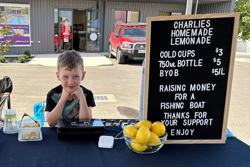 A boat stand at his lemonade stand, decorated with yellow and green flags. 