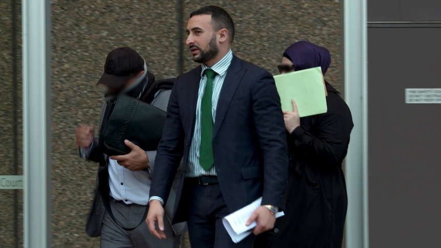 a man in a suit walking out of a building with a mother and father covering their faces