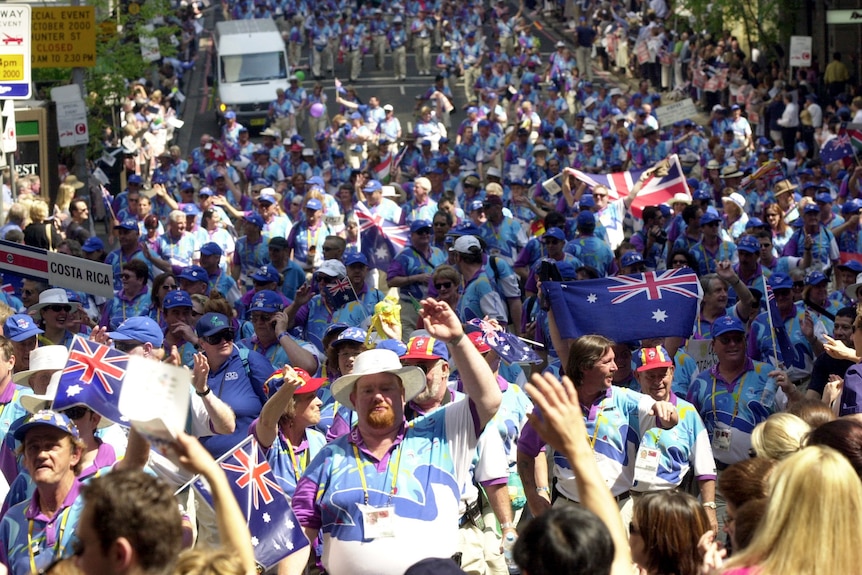 A huge crowd streteches down the street. Everyone is wearing Sydney 2000 apparel . Some people are waving Australian flags. 