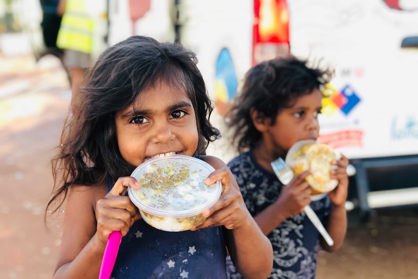 Two young dark-skinned children holding plastic containers of food.