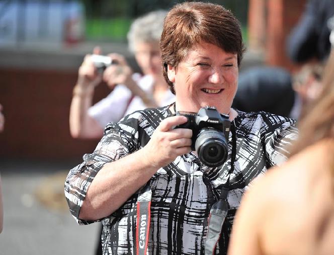 A smiling woman wearing a black and white shirt holds a camera.