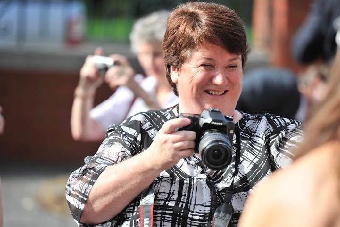 A smiling woman wearing a black and white shirt holds a camera.