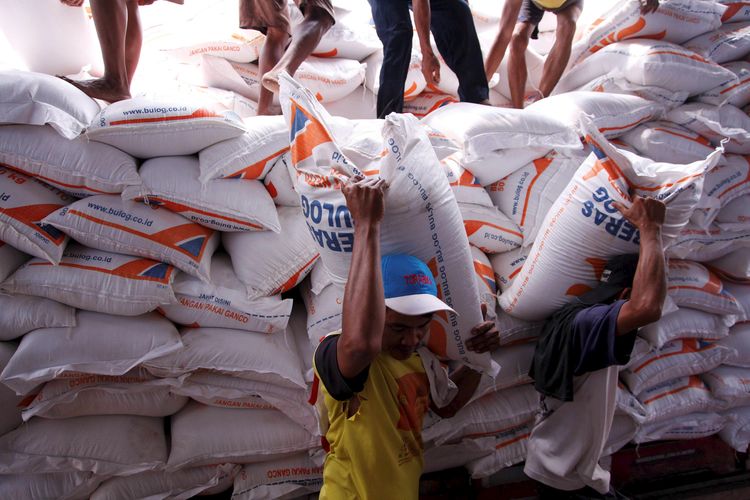 Two men carrying sacks of rice on their shoulders in a traditional market