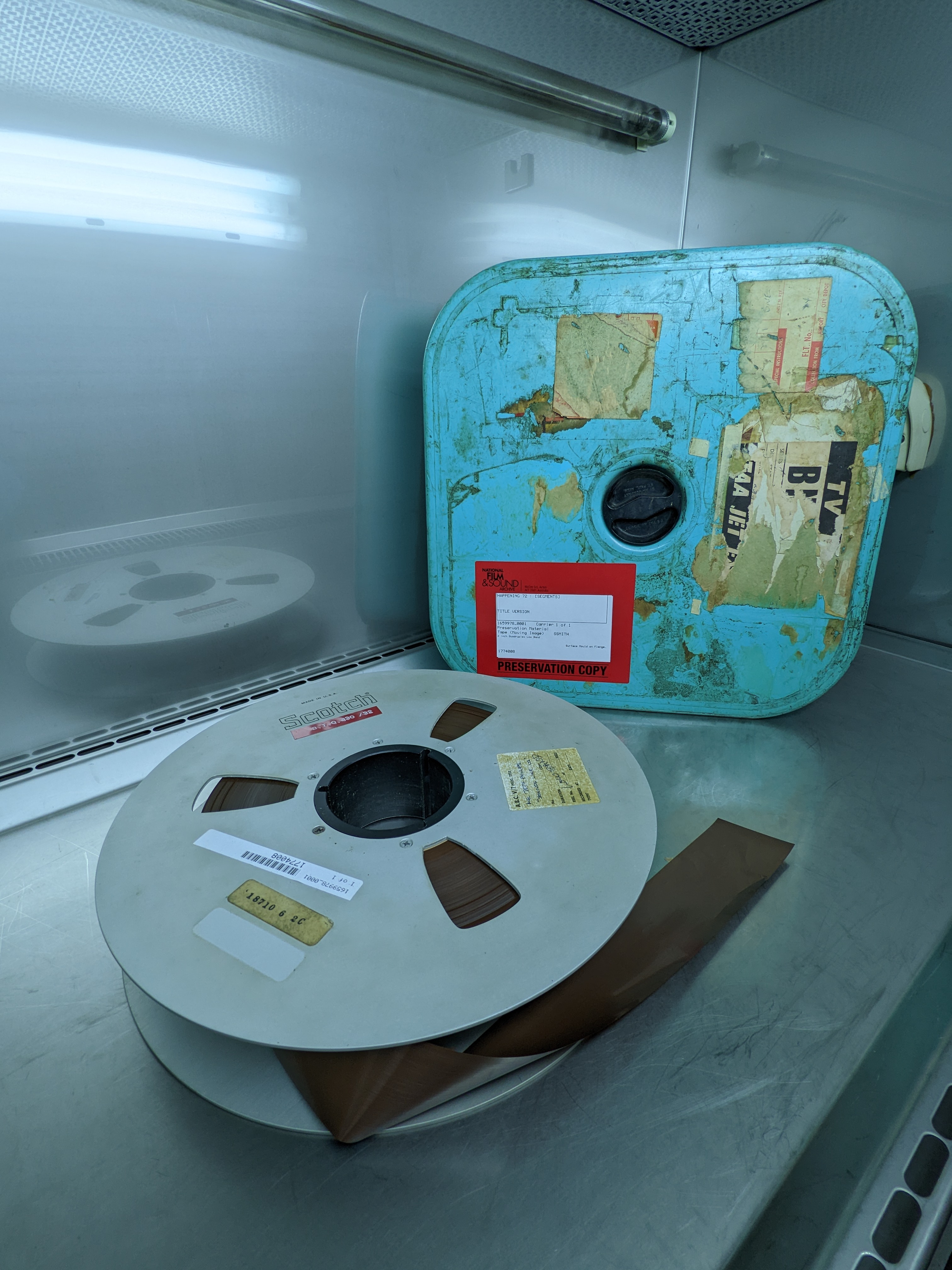 A two-inch reel lying beside a battered, upright case with a bright red label.