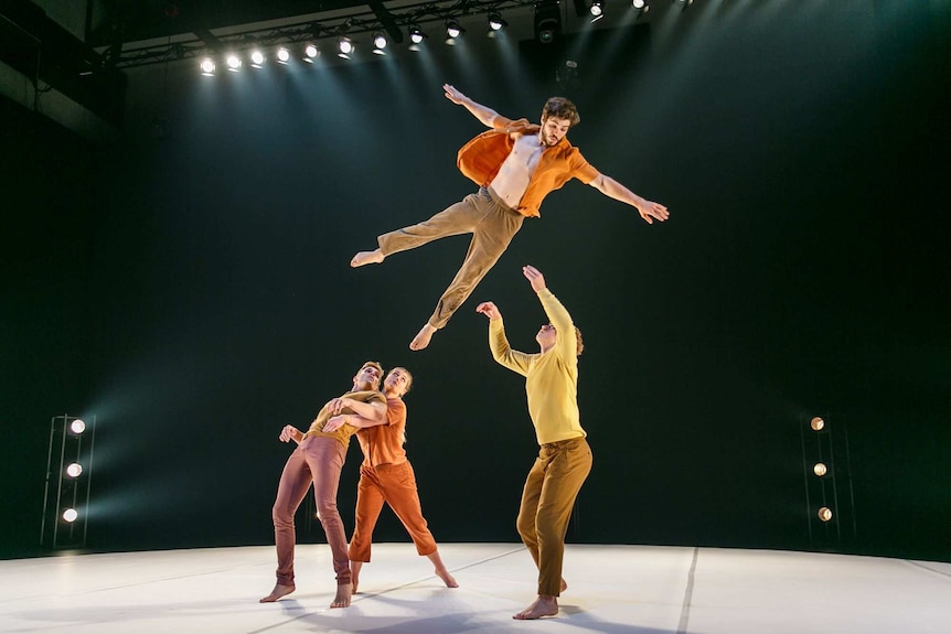 Acrobats on stage in a Circa performance, with one leaping in the air about to be caught in another's arms