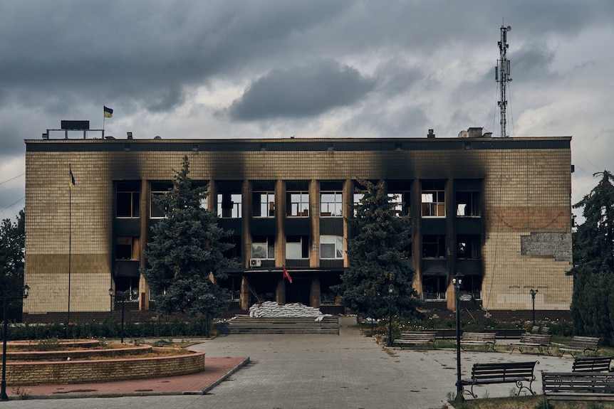 A Ukrainian flag waves above the charred shell of a brick town hall building.