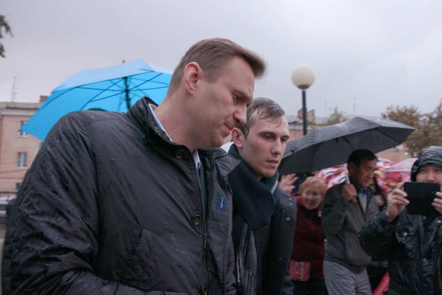 Alexei Navalny is escorted into the rally held in an open public park