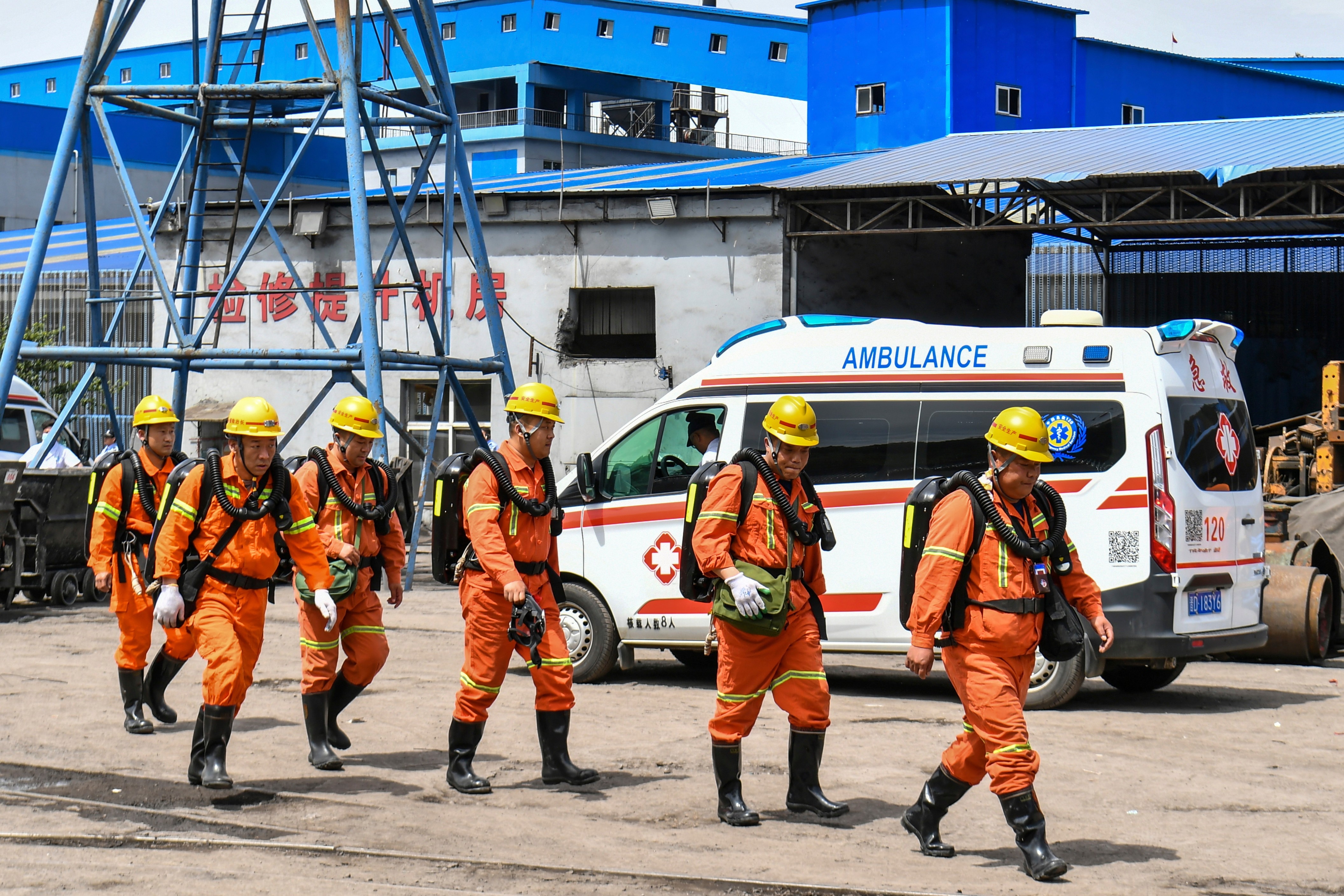 Several people in orange jumpsuits with yellow hard hats.