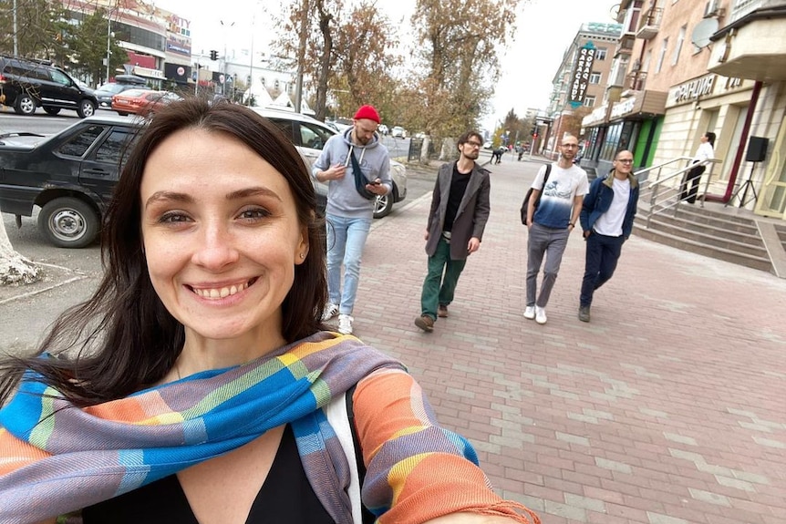 Smiling white brunette woman taking selfie on city street.